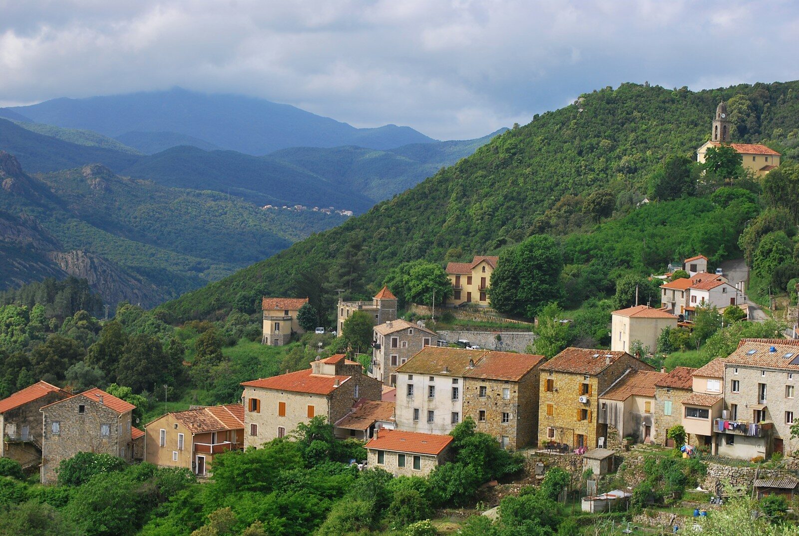 a small village on a mountain side with mountains in the background