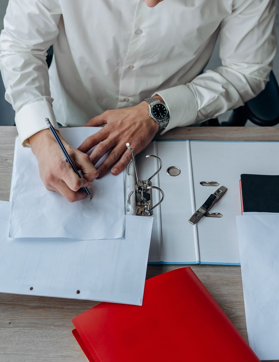 An adult writing in a binder at a desk with office supplies.