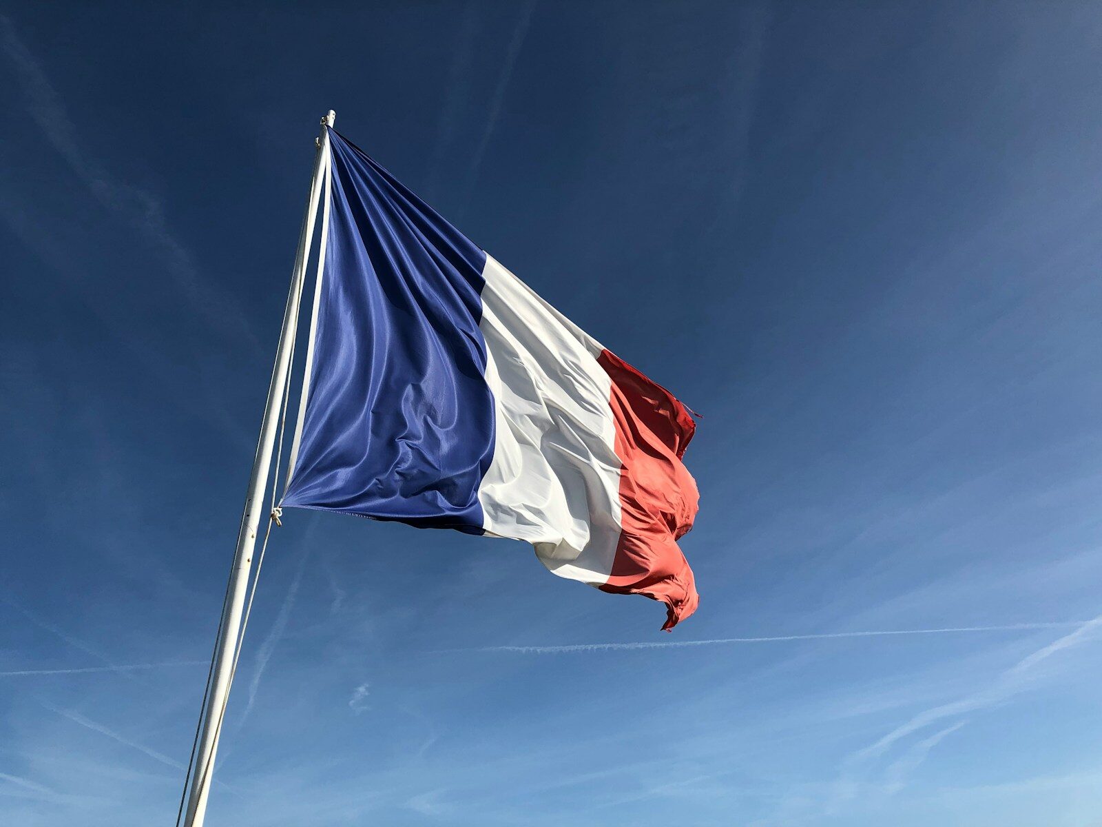 The French flag waving on a flagpole against a clear blue sky